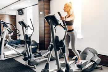 A lady working out on an elliptical machine at a gym